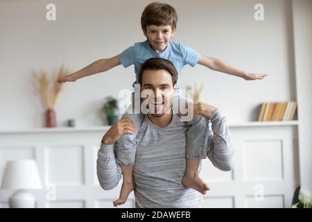 Funny portrait little boy pretending flying sitting on fathers shoulders Stock Photo