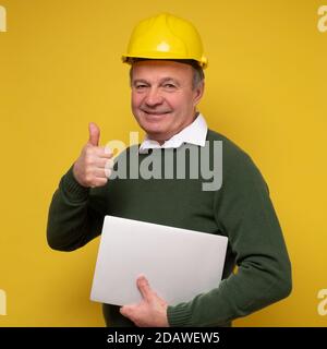 Senior man with special hard hat working using laptop approving showing thumb up Stock Photo