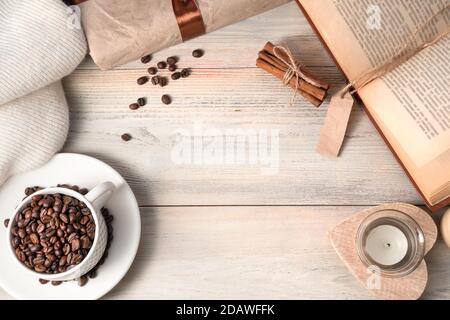 Cozy background with coffee beans in a white Cup, sweater, book, gift on a light wooden table. Stock Photo