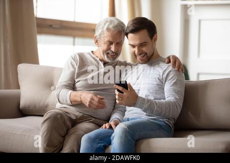 Happy older father and son using phone at home together Stock Photo