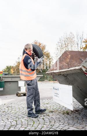 Man putting old tire in container of recycling center Stock Photo