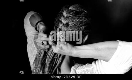 A woman is braiding herself a braid of dreadlocks. Stands with his back, fingers are visible. Stock Photo