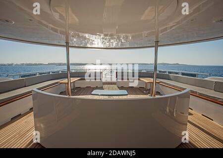 Teak stern wooden deck of a large luxury motor yacht with chairs sofa table and tropical sea view background Stock Photo