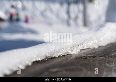 Wooden railing covered with crispy snow on sunny day in winter. close-up with blurred background. Stock Photo