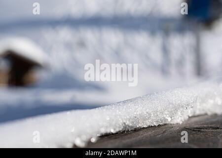 Wooden railing covered with crispy snow on sunny day in winter. close-up with blurred background. Stock Photo