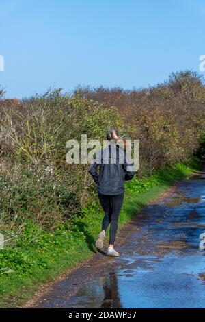 a young attractive fit woman dressed in running gear running along a country lane or track to keep fit.on a bright sunny day Stock Photo