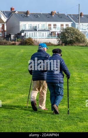 an elderly couple using walking sticks walking on a bright sunny autumn day at yarmouth on the isle of wight Stock Photo