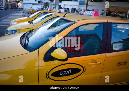 Cordoba, Argentina - January, 2020: Yellow taxi cars parked on parking lot in a row on a gas station. Currency exchange rates neon lights Stock Photo