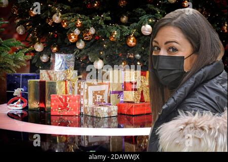 FOTOMONTAGE-Weihafterten 2020 in the middle of the coronavirus pandemic. What about the partial lockdown? Loosening of detainees will probably only be done with significantly decreasing corona numbers. Young woman with face mask, mask in front of Weihaftertsbaum, Weihaftertsbaum, Christmas tree, Christmas tree, Christmas tree, decorated, Christmas tree ball. Gifts, packages. | usage worldwide