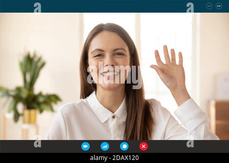 Smiling pretty millennial woman making hello gesture, starting online conversation. Stock Photo