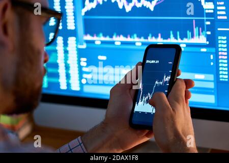 Trader using mobile phone app analytics for stock trading graph data analysis. Stock Photo