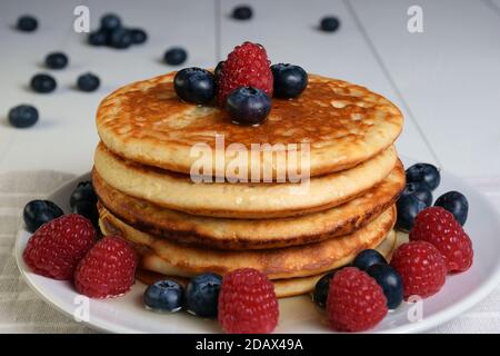 Plate of pancakes with maple syrup, blueberries and raspberries on white wooden table. Stock Photo