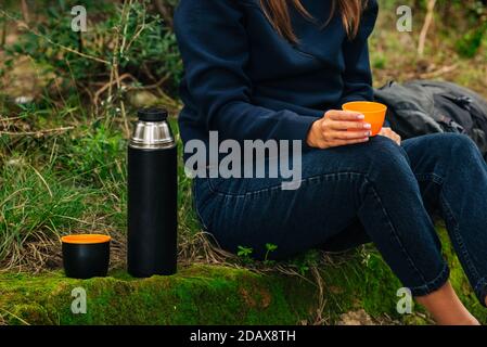 Woman drinking tea from thermos during hike outdoors. Refreshment during hiking in the woods Stock Photo