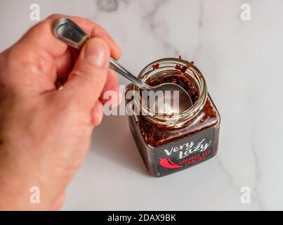 Norwich, Norfolk, UK – November 15 2020. Illustrative editorial photo of an unidentifiable human hand holding a spoon with a glass jar of Very Lazy co Stock Photo