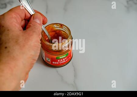 Norwich, Norfolk, UK – November 15 2020. Illustrative editorial photo of an unidentifiable human hand holding a spoon with a glass jar of Asda Easy Re Stock Photo