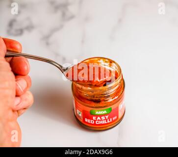Norwich, Norfolk, UK – November 15 2020. Illustrative editorial photo of an unidentifiable human hand holding a spoon with a glass jar of Asda Easy Re Stock Photo