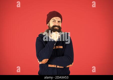 Personal stylist. Warm and comfortable. Fashion menswear shop. Masculine clothes concept. Think and decide. Winter menswear. Man bearded warm jumper and hat red background. Winter season menswear. Stock Photo