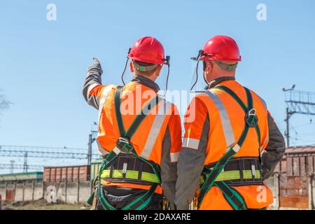 Two working electricians look at the high voltage power lines and railway cars shows his hand Stock Photo
