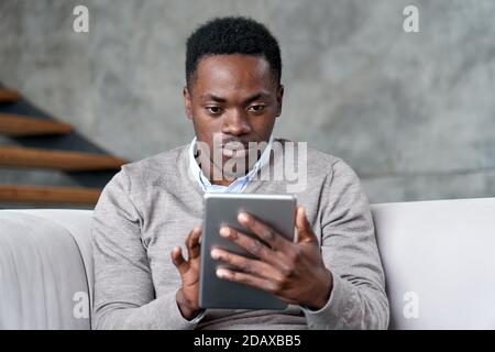 Young adult african man using digital tablet apps on computer at home. Stock Photo