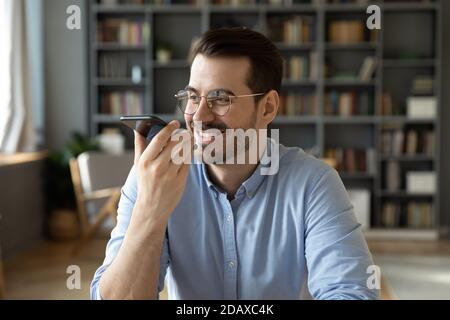 Smiling businessman sit in office holding smartphone leaves voice message Stock Photo