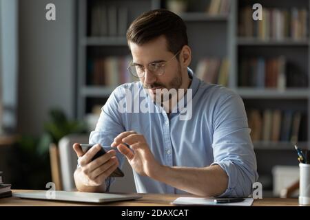 Serious businessman wearing spectacles using mobile phone sit at desk Stock Photo