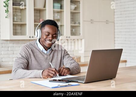 Black male student wearing headphones elearning on laptop at home office. Stock Photo