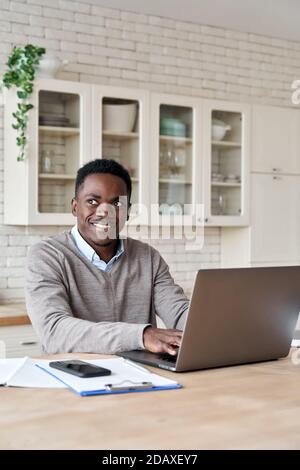 Smiling african american man using laptop working from home office, vertical. Stock Photo