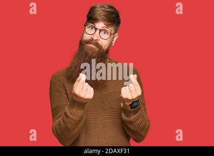 Young irish redhead man wearing casual clothes and glasses doing money gesture with hands, asking for salary payment, millionaire business Stock Photo