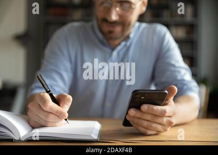 Businessman sitting at desk holding smartphone writes schedule in organizer Stock Photo