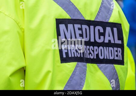 Medical first responder wearing a bright yellow coat with a grey reflective cross. The person is back on to the camera. Stock Photo