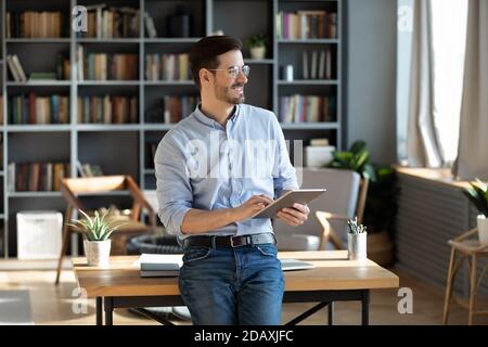 Entrepreneur holding tablet device looks out the window feels happy Stock Photo