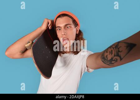 Young adult man holding skateboard making silly self portrait Stock Photo