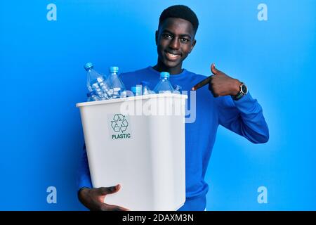 Young african american man holding recycling wastebasket with plastic bottles pointing finger to one self smiling happy and proud Stock Photo