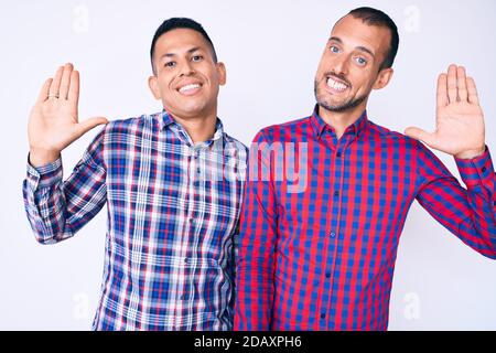 Young gay couple of two men wearing casual clothes waiving saying hello happy and smiling, friendly welcome gesture Stock Photo