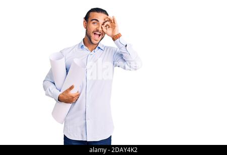 Young handsome man holding paper blueprints smiling happy doing ok sign with hand on eye looking through fingers Stock Photo