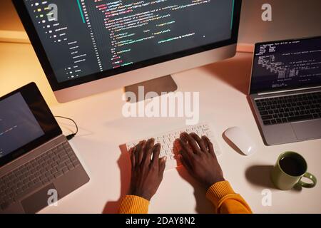 Top view close up of unrecognizable African-American man writing code while working with multiple computer screens, copy space Stock Photo