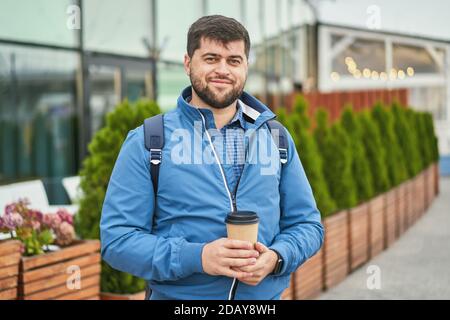 Young man with takeaway coffee in paper cup walks outdoor. Stock Photo