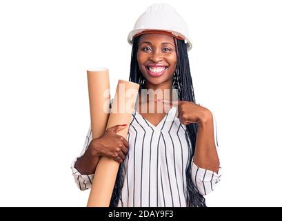 Young african american woman wearing architect hardhat holding blueprints smiling happy pointing with hand and finger Stock Photo