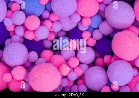 Background from multi-colored pom-poms of different sizes. Pink, violet and violet furry pom-pons in a heap close-up. Stock Photo