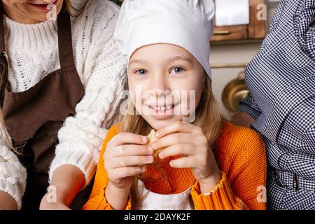 The family prepares gingerbread cookies in the kitchen.  Grandma, mom and daughter bake cookies in the kitchen and decorate cookies on Christmas Eve. Stock Photo