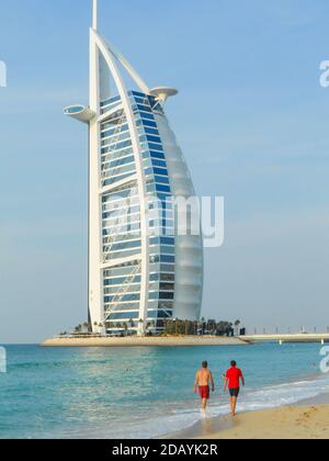 Two men stroll on the beach in front of the Burj Al Arab building in Dubai UAE Stock Photo