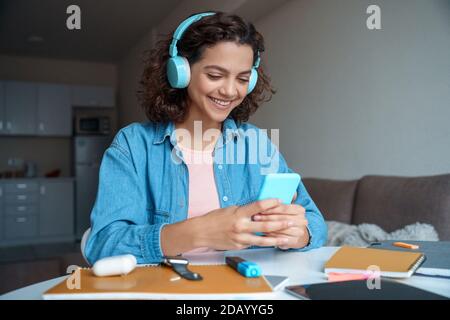 Hispanic young woman in earphones using smartphone app. Stock Photo
