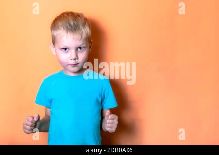 boy in a blue t shirt on a pink background looks at the camera lens clenching his fists Stock Photo