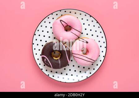 Classic chocolate, strawberry donut on white round plate with black peas isolated on pink background Flat lat lay Top View Knolling Unhealthy and Stock Photo