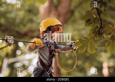 Happy child climbing in the trees. Children summer activities. Early childhood development. Child. Safe Climbing extreme sport with helmet Stock Photo