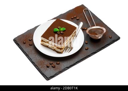 Traditional Italian Tiramisu square dessert portion on ceramic plate, strainer and coffee beans on stone serving cutting board isolated on white Stock Photo