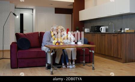 Senior grandpa and grandma with child girl granddaughter spending time home together, sitting on sofa in the living room, using mobile phone. Playing games, making selfie photos together on smartphone Stock Photo