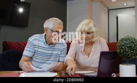 Worried senior retired couple checking calculating bills bank loan payment doing paperwork discuss unpaid debt taxes, stressed old grandparents family look at laptop upset about money problem concept Stock Photo