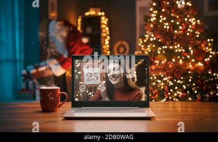 Woman showing the calendar on a video call and Santa Claus bringing gifts in the background Stock Photo