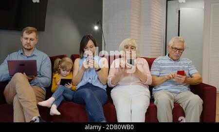 Addicted to gadgets family using mobile phone, tablet, laptop ignoring each other at home. Senior couple, woman, man, child girl involved in chatting in social networks, internet obsession concept Stock Photo